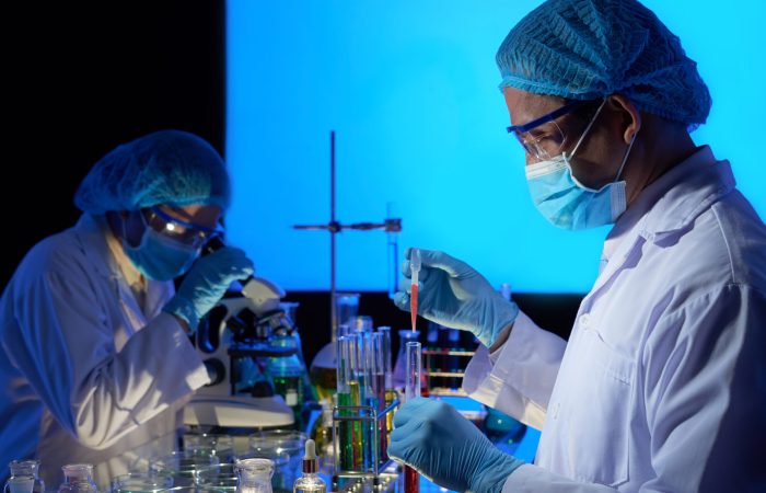 Asian Scientists Working on Vaccine Creation Gifted Asian scientist wearing rubber gloves and safety masks working together on creation of cancer vaccine, interior of dark laboratory on background
